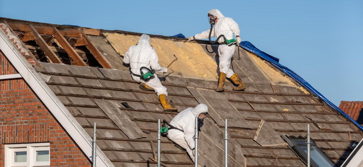 Techniciens en combinaison de protection réalisant un désamiantage de toiture